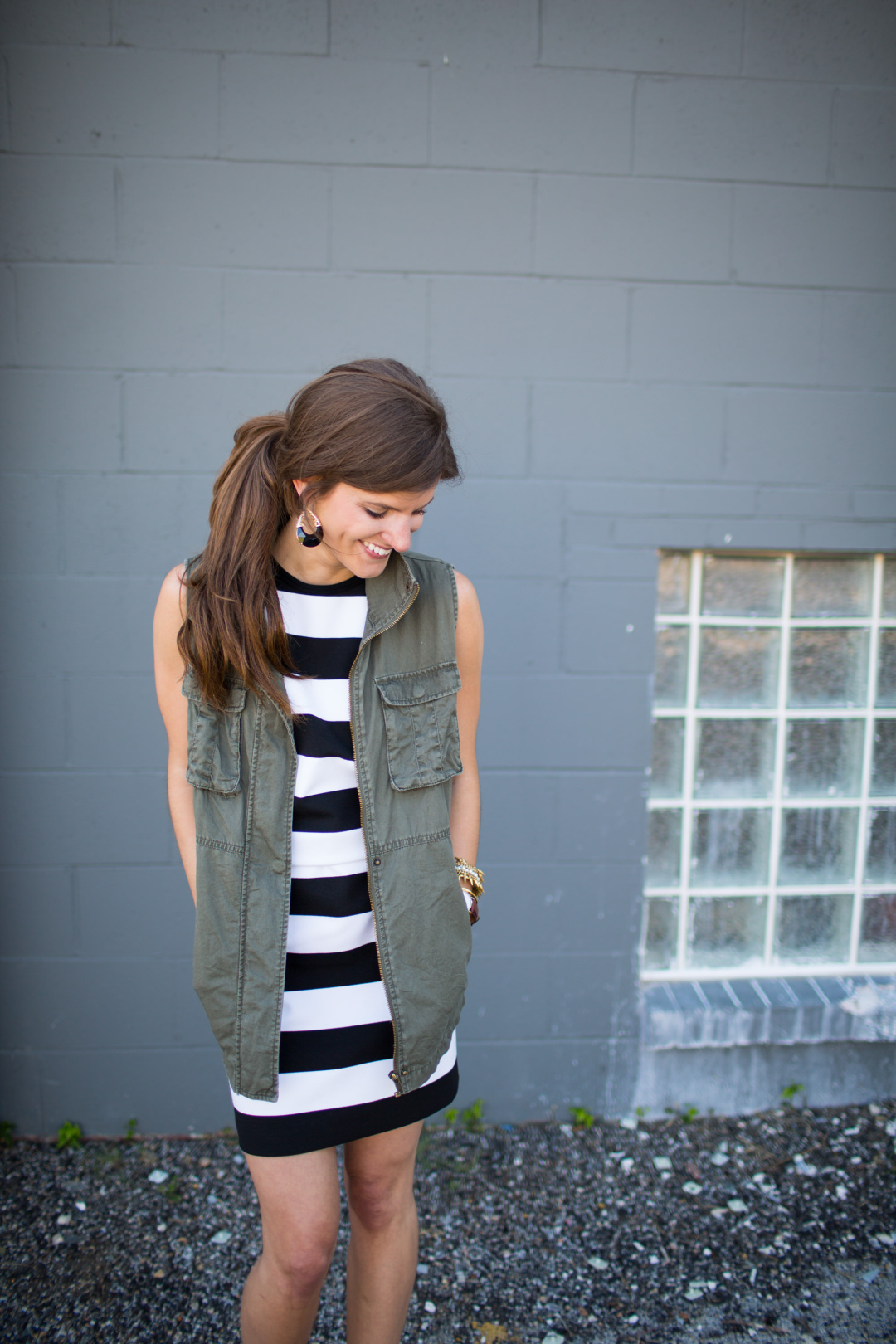transitional fall outfit idea, olive green utility vest, striped dress, lace up black heels, kendra scott earrings, gigi ny neutral teddy tote, going out outfit, military vest, black and white stripe dress