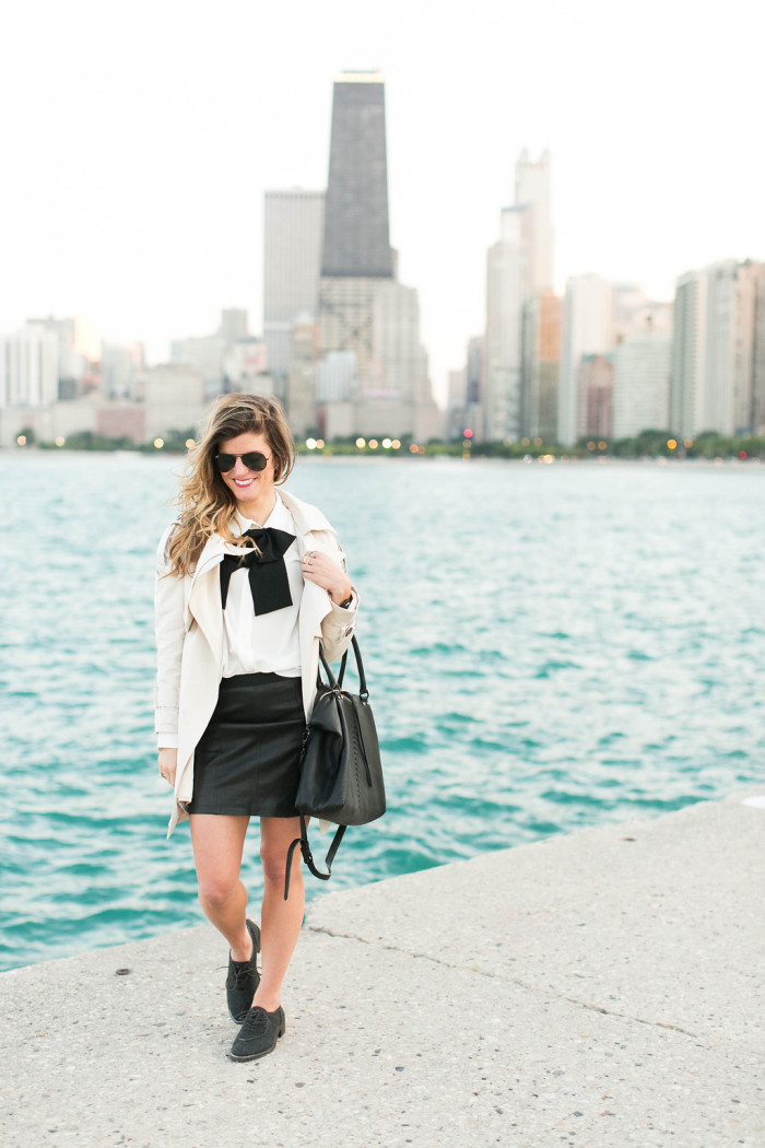 leather mini skirt worn with a white blouse and black bow tie with a basic trench coat