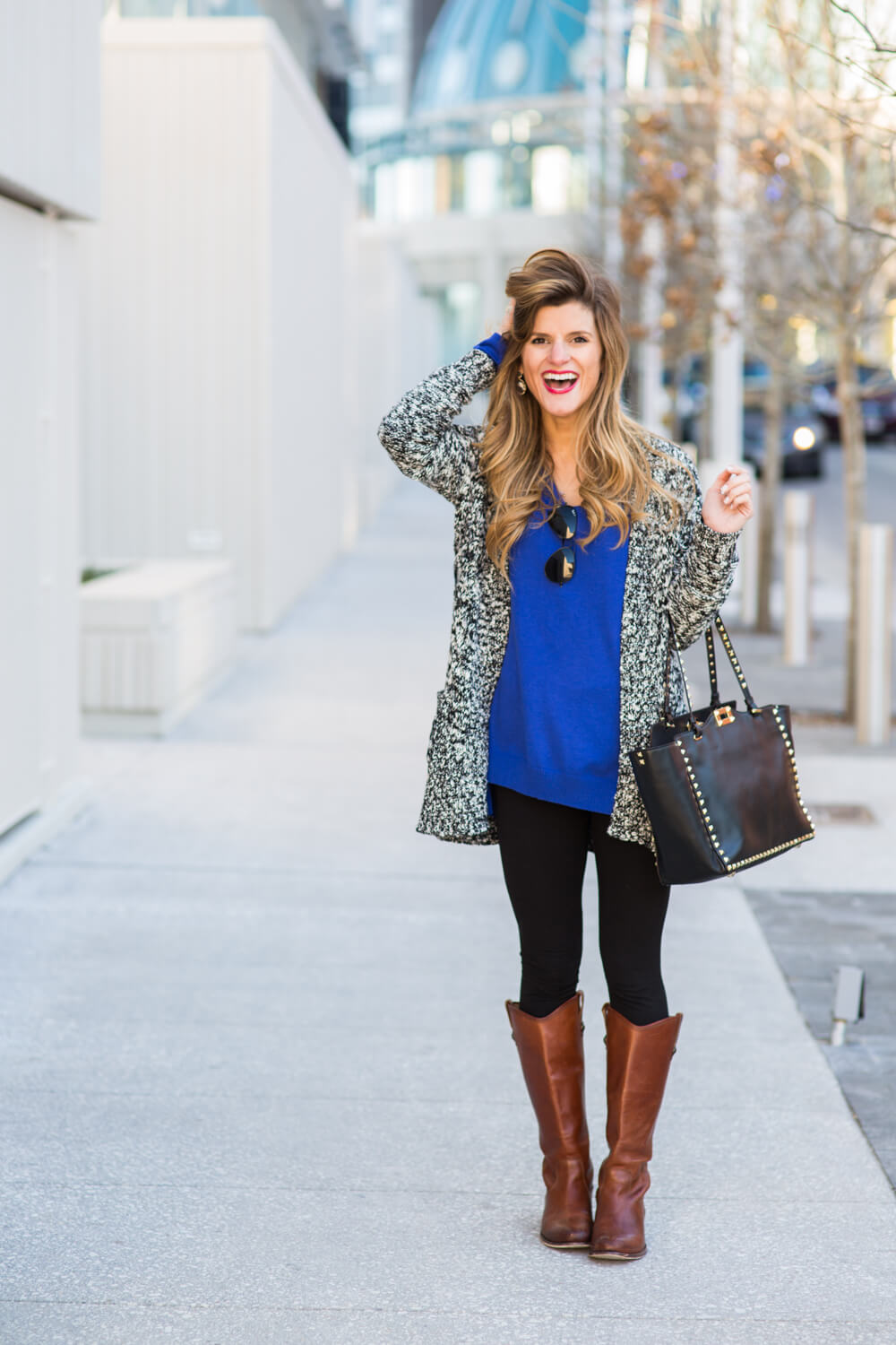 Brighton wearing cardigan over a blue sweater with black ray-ban aviators and kendra scott bar necklace 