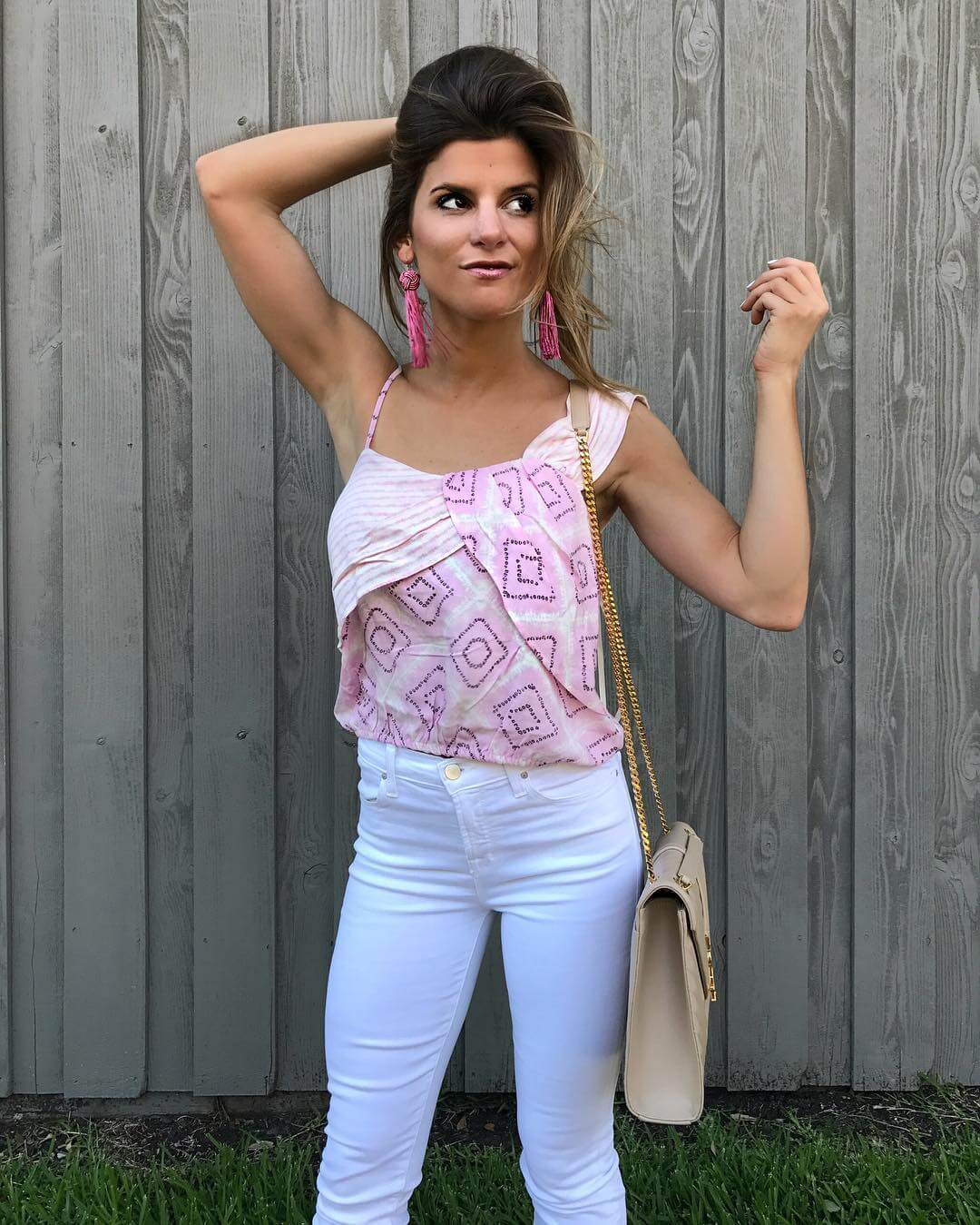 brighton keller wearing asymmetrical pink printed top with white jeans and pink earrings 