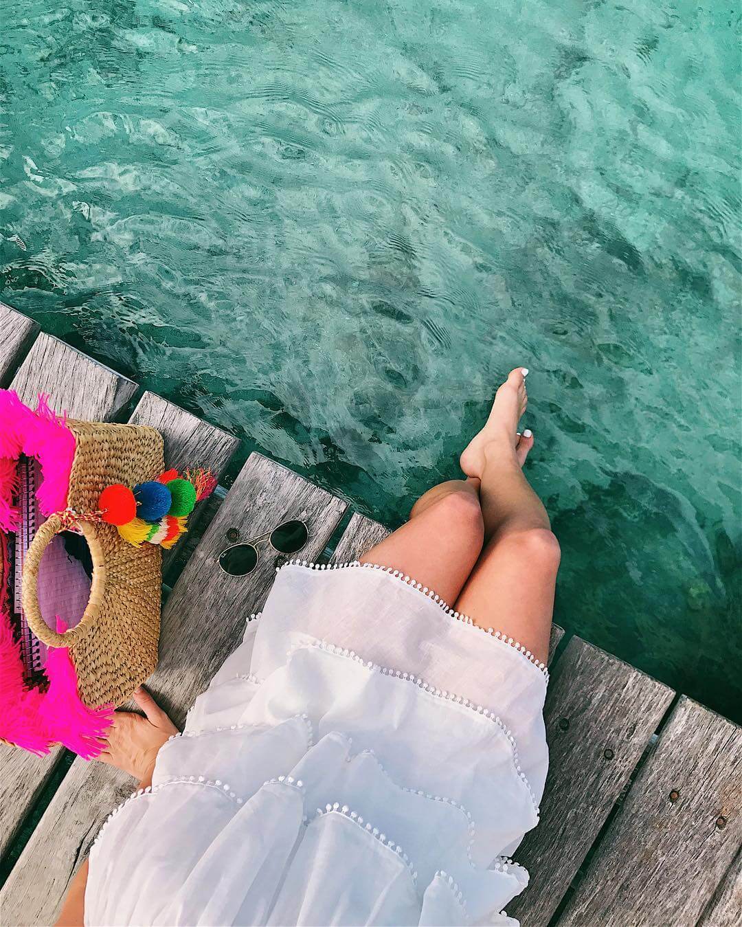brighton keller overlooking the water in fiji wearing ruffled white dress and pom pom beach bag 