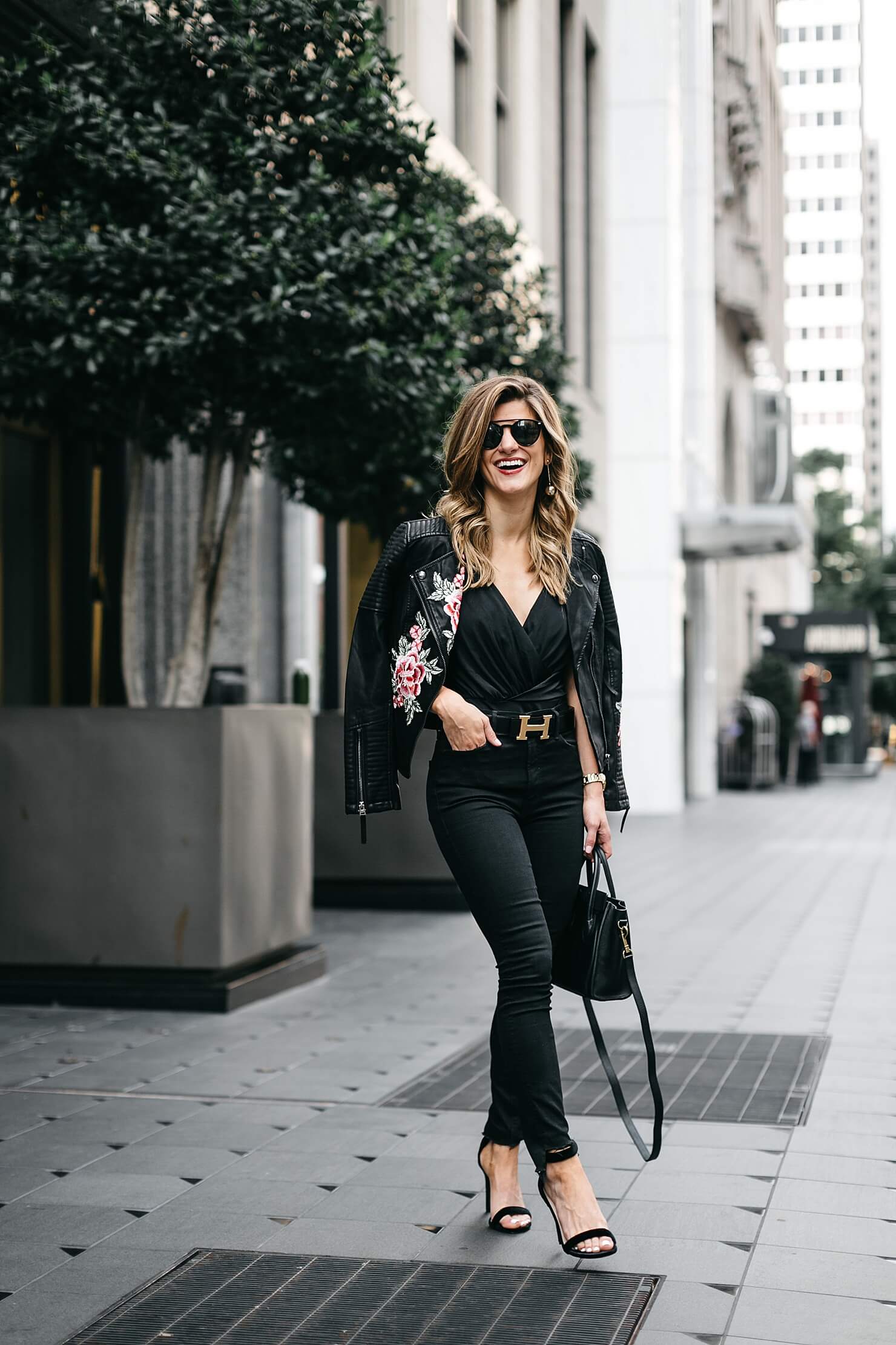 all black bodysuit outfit with embroidered leather jacket, black jeans, statement belt, and heels