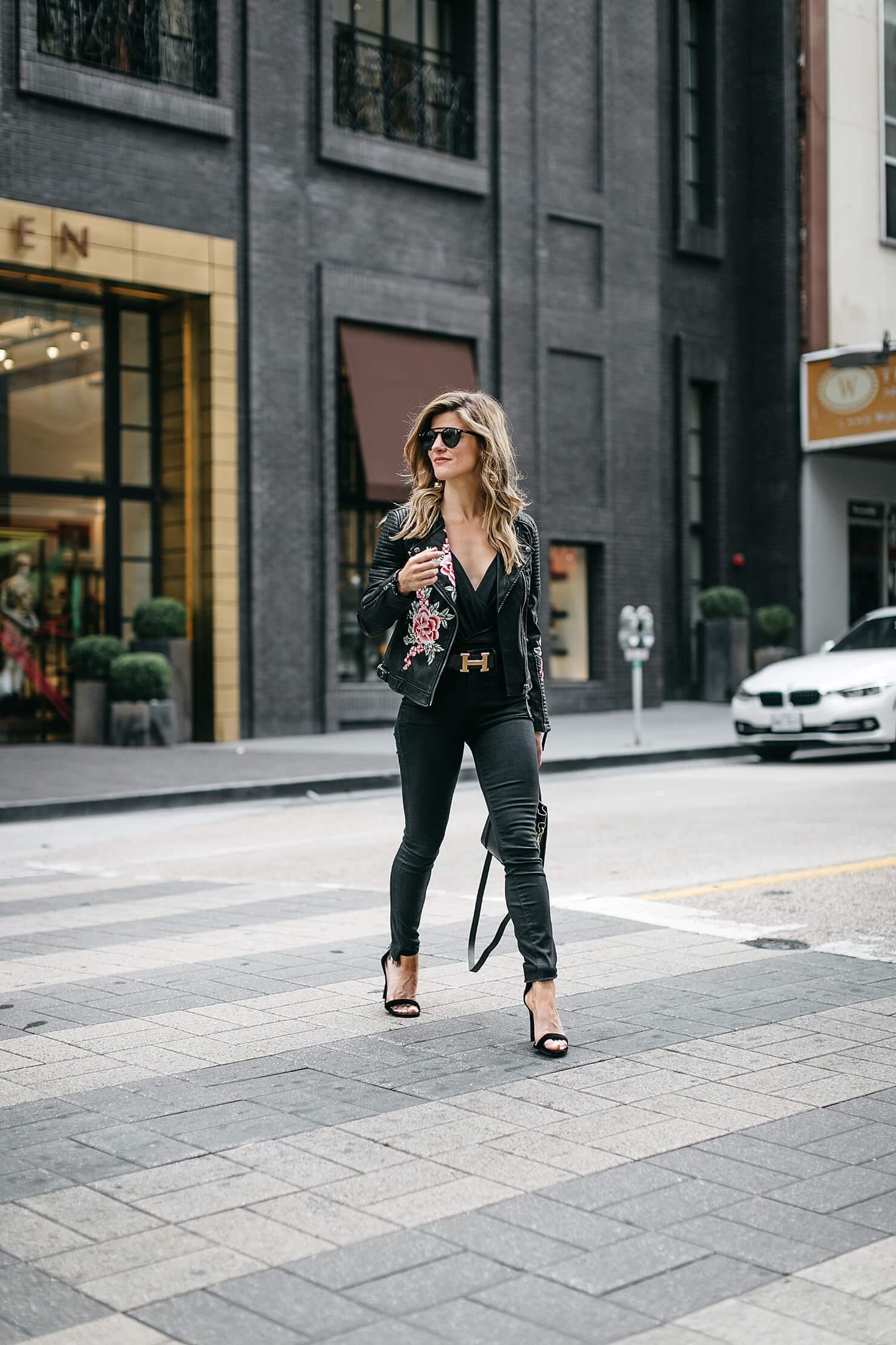 all black bodysuit outfit with embroidered leather jacket, black jeans, statement belt, and heels