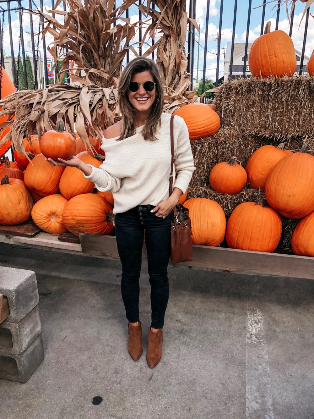 brighton keller at pumpkin patch wearing cream sweater black jeans and tan booties with bucket bag and sunglasses