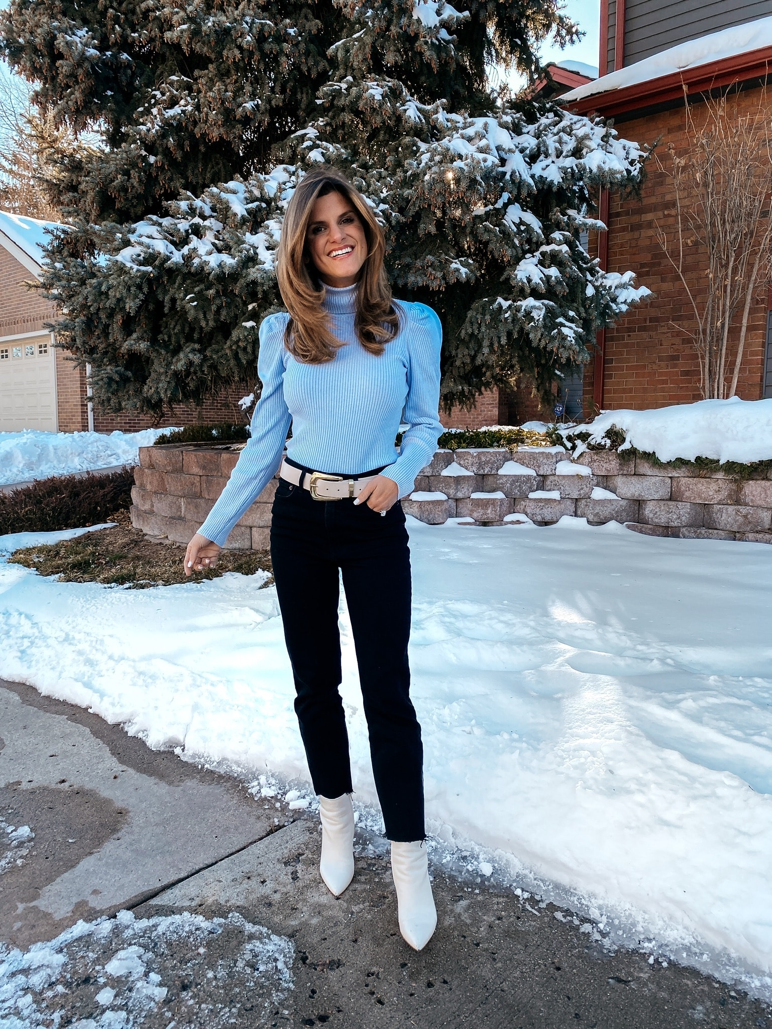 Brighton Butler in blue sweater, white belt, black jeans and white booties